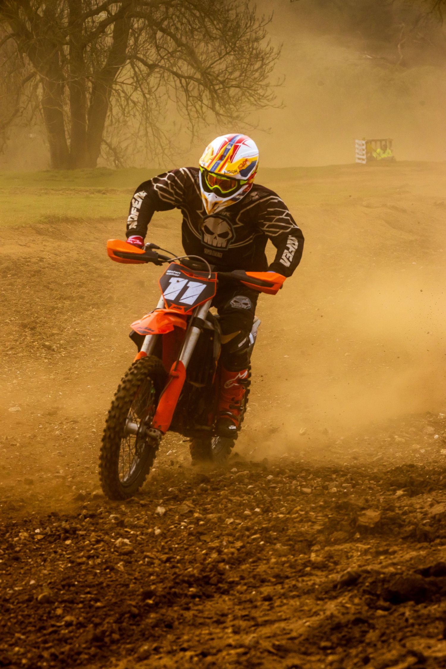Motocross rider in black gear racing an orange dirt bike on a dusty track, kicking up clouds of dirt. Action shot taken by photographer Rod