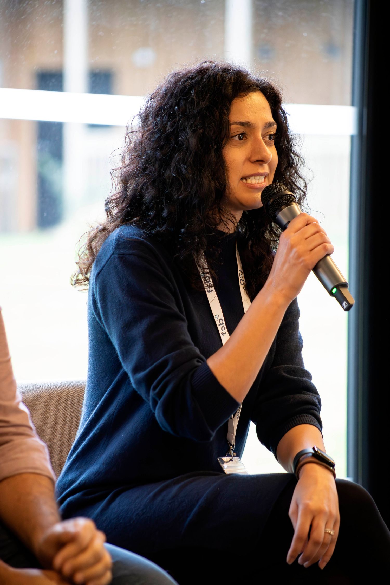 Woman with curly hair speaking into microphone at a panel discussion event.