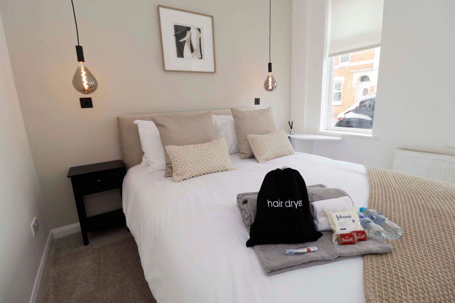 Cozy modern bedroom with white bedding, pendant lights, and a hair dryer bag on the bed.