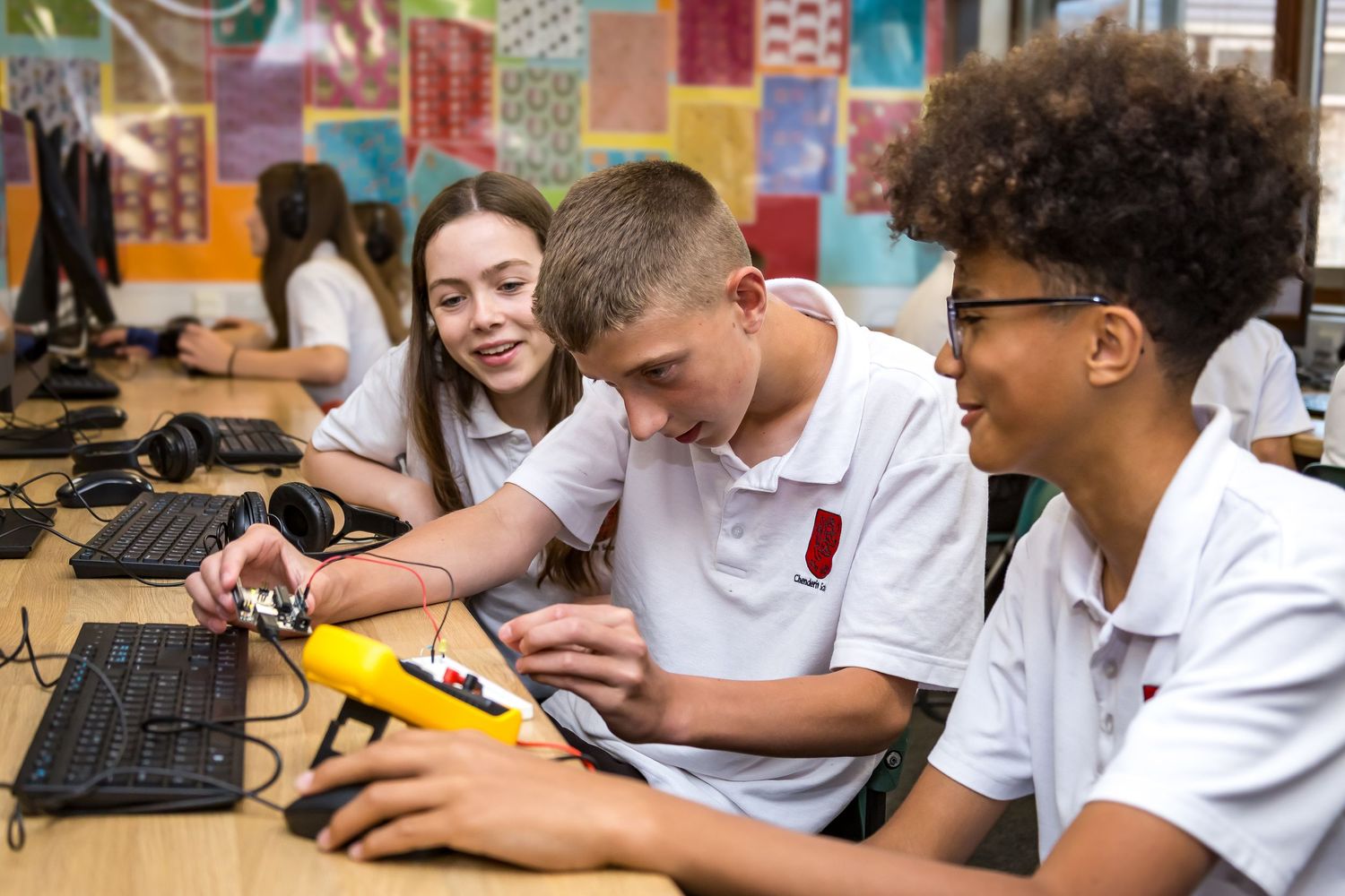 Three secondary school students working together on electronics at a computer lab desk.