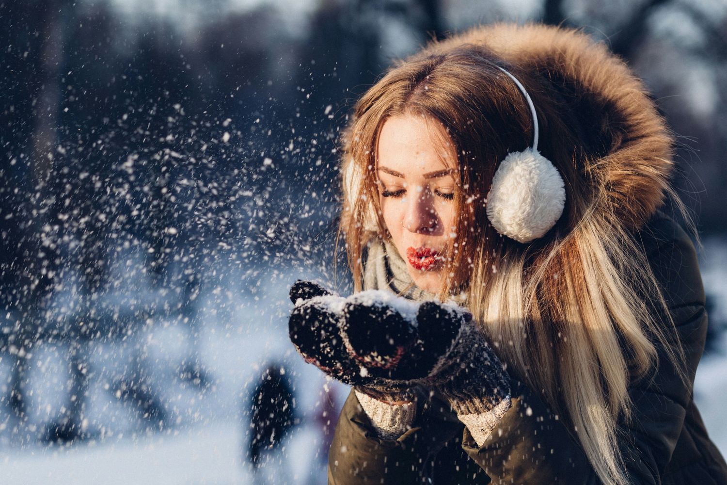 Winter portrait of person blowing snow while wearing fur-trimmed ear muffs.