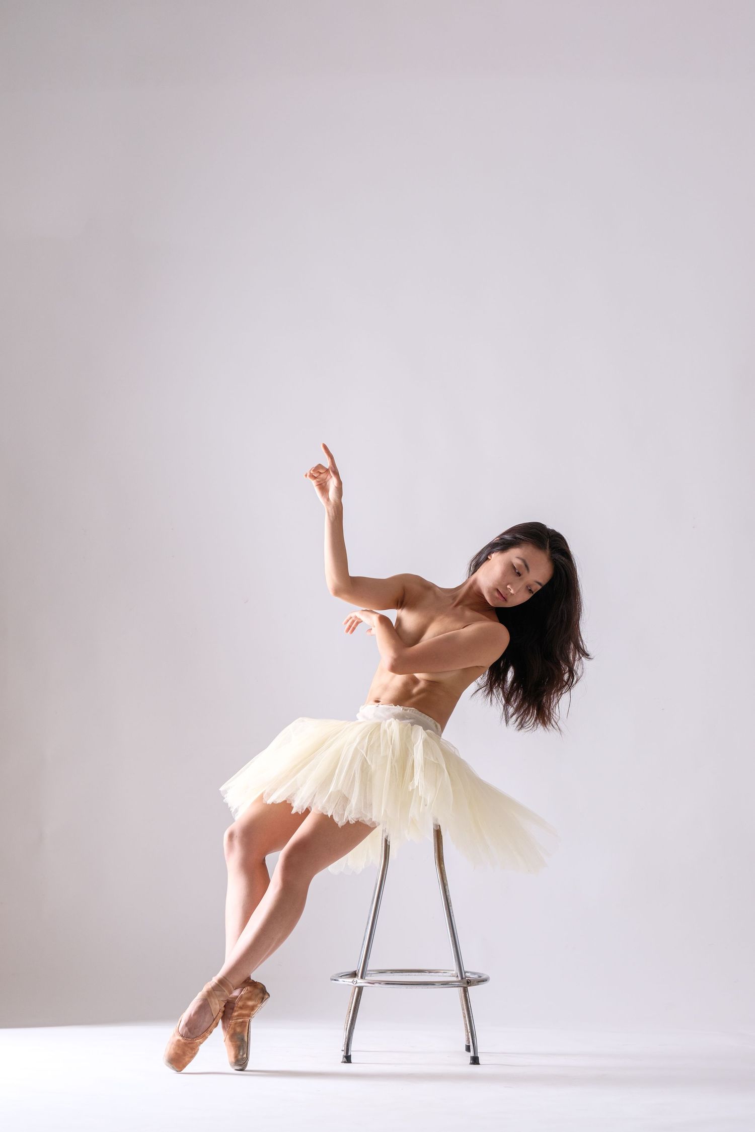 Contemporary ballet dancer performs expressive movements with chair in bright studio space.