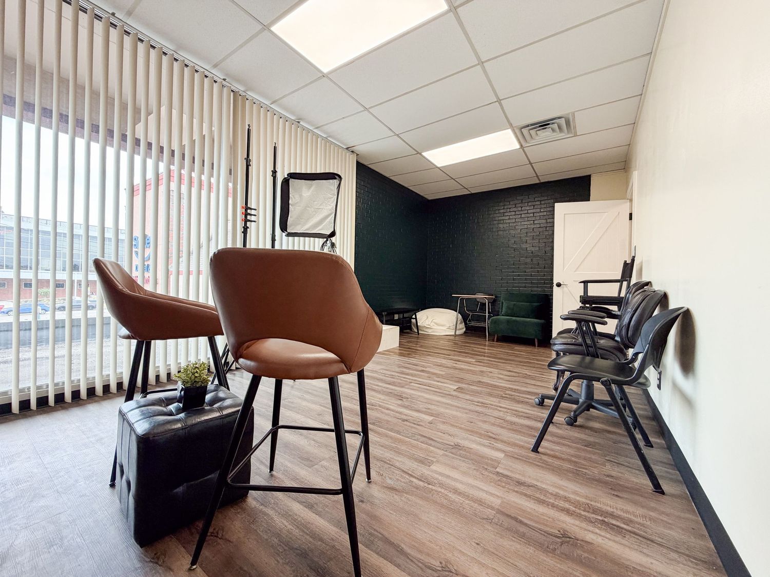 Modern office waiting room with brown leather chairs, hardwood floors, dark accent wall, and vertical blinds by a window.