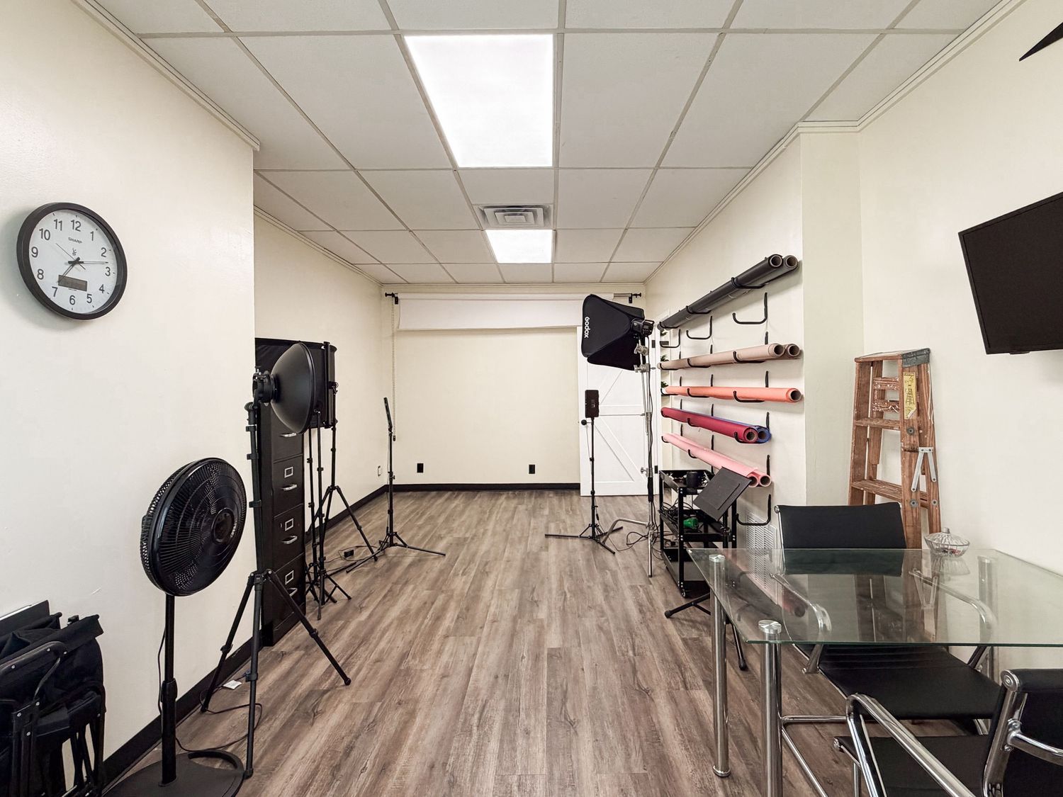 Professional photography studio with lighting equipment, hardwood floors, a wall clock, and a mounted TV screen.