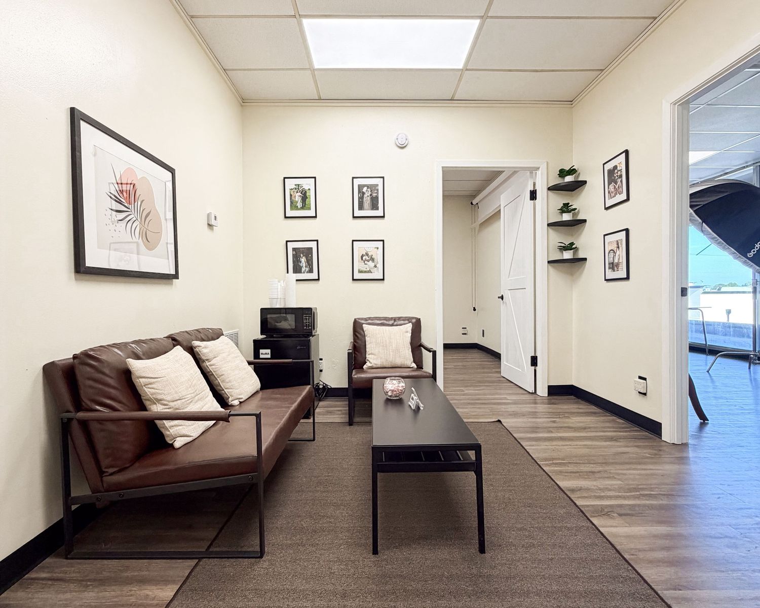 Modern waiting room with brown leather sofa, coffee table, framed wall art, and hardwood floors in a professional office.