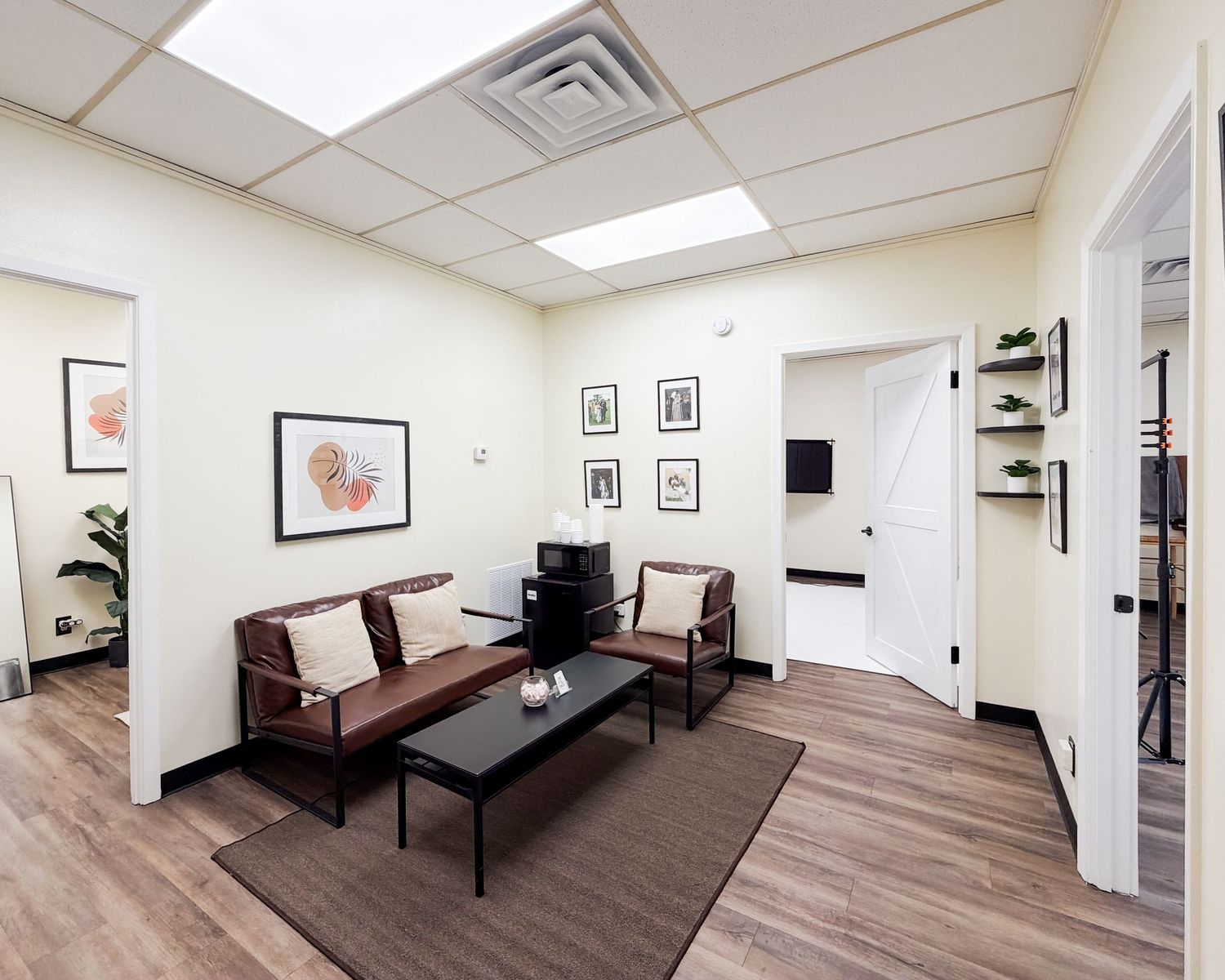 Modern medical waiting room with brown leather sofas, coffee table, wood floors, and neutral walls featuring framed artwork.