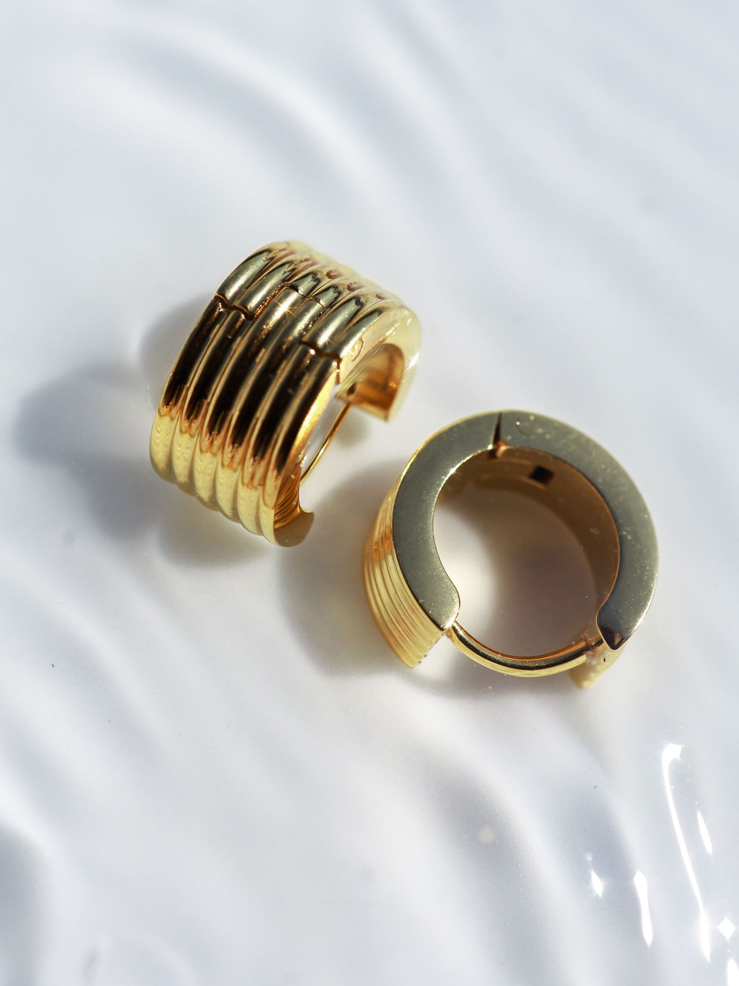 Gold ribbed huggie hoop earrings with a wide band design, displayed on a white surface.