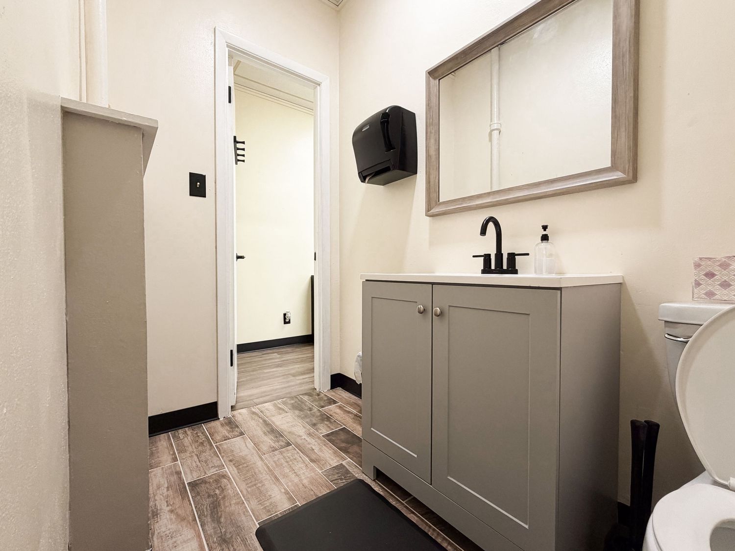 Modern bathroom with gray vanity, medicine cabinet mirror, wood-look floors, and open door leading to hallway.