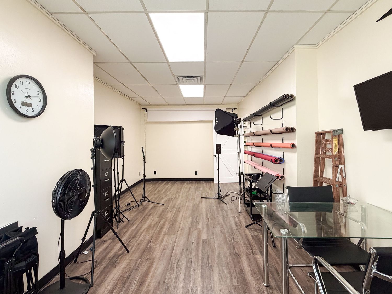 Professional photography studio with lighting equipment, hardwood floors, a wall clock, and a flat-screen TV mounted on the wall.