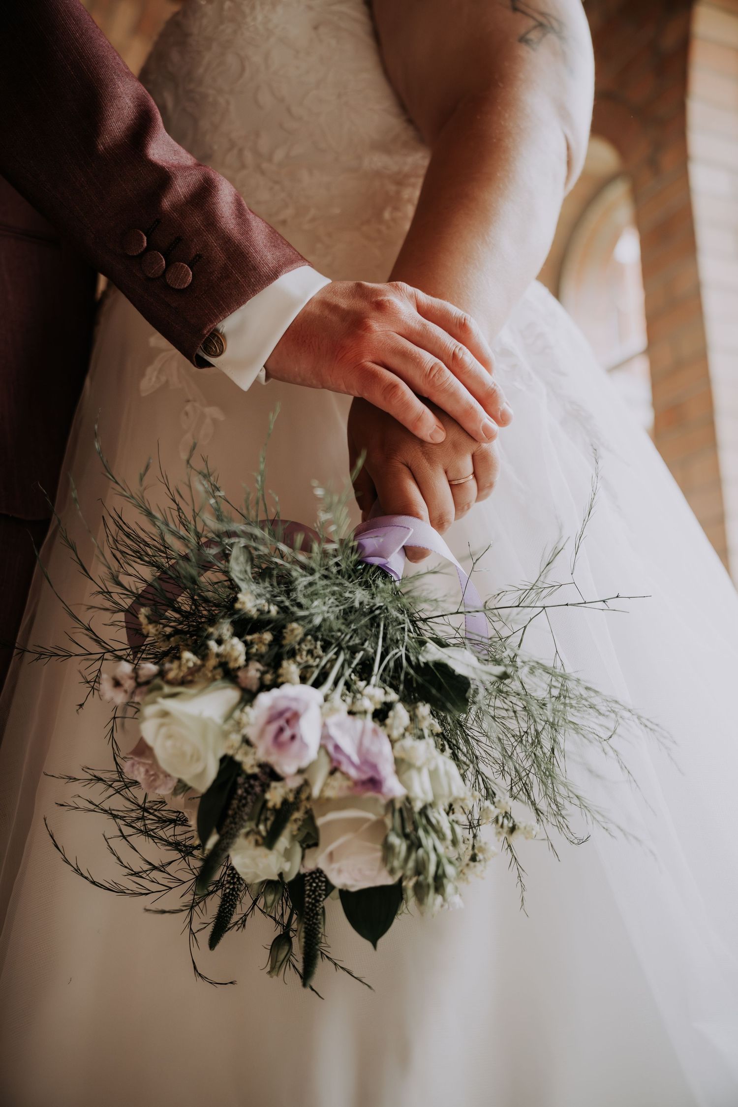 Bride and groom holding a rustic bouquet of white and lavender roses with wild greenery on their wedding day.