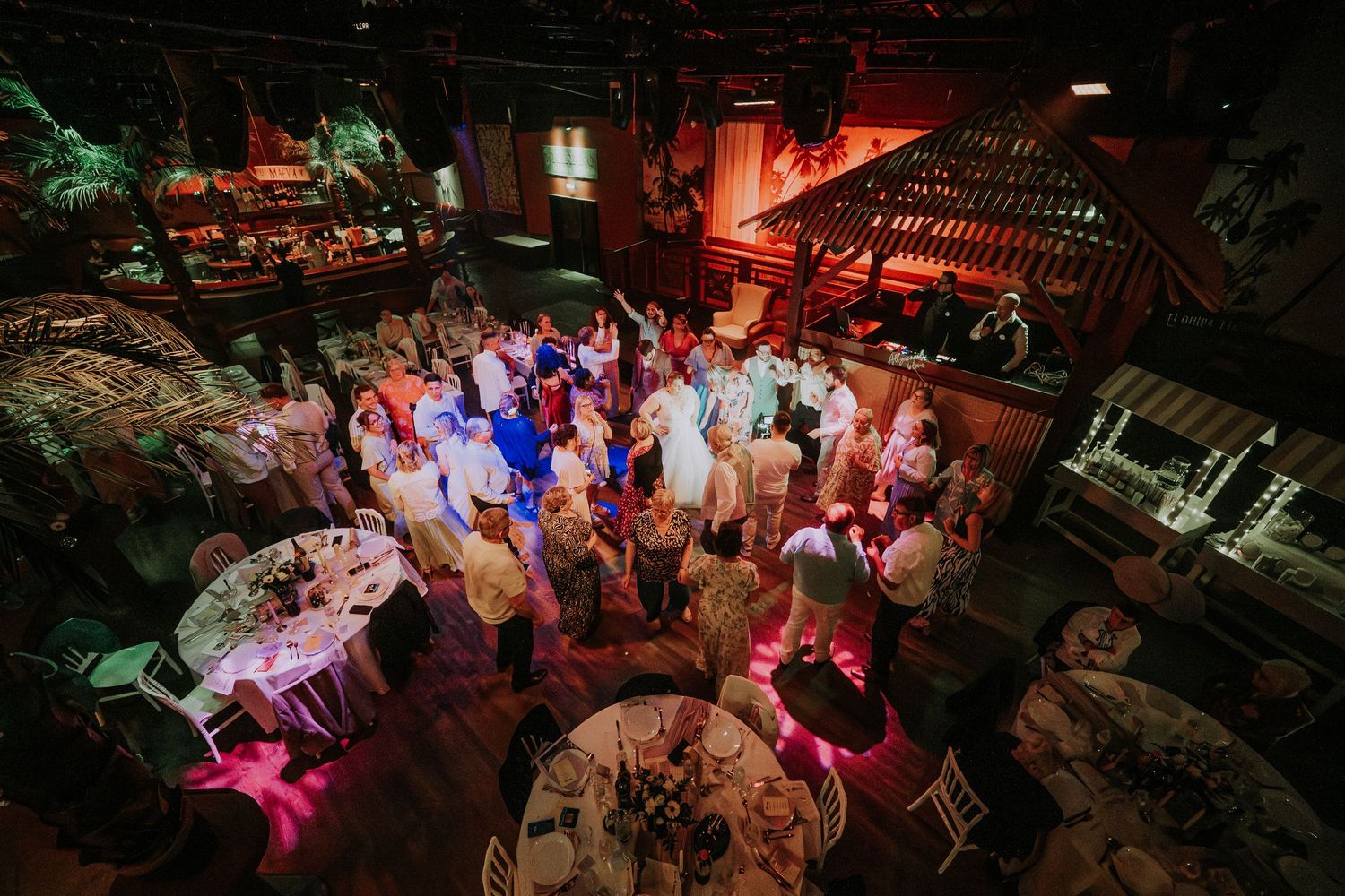 Aerial view of elegant wedding reception with guests mingling around decorated tables in a warmly lit venue.