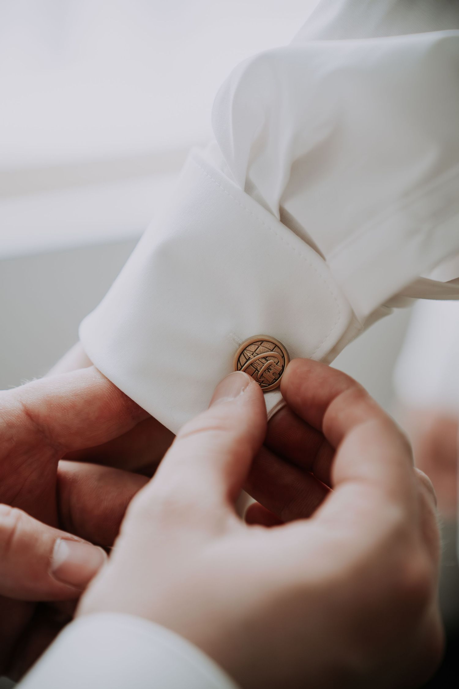 Hands fastening a gold cufflink on a white dress shirt sleeve for a formal occasion.