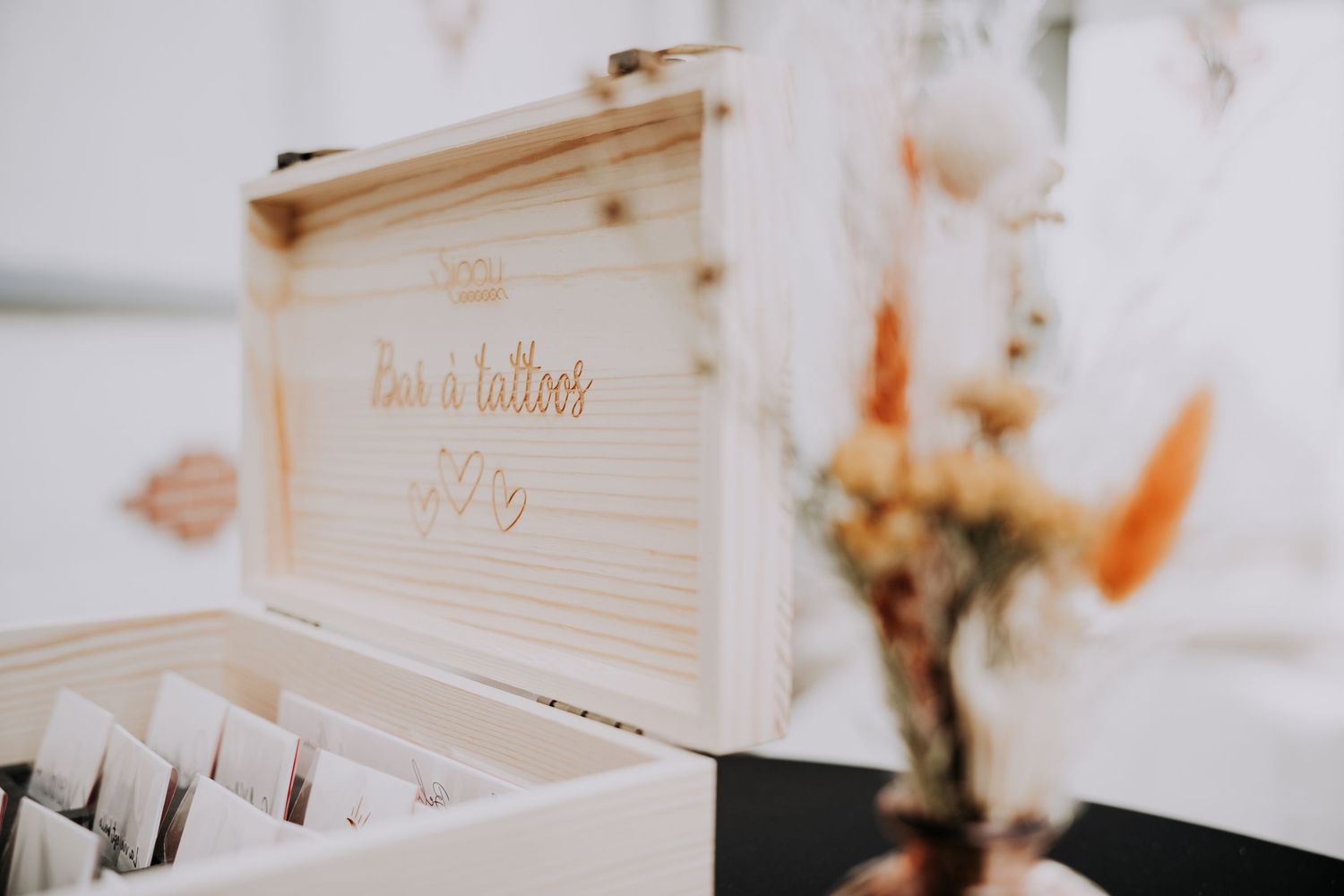 Wooden keepsake box with engraved script lettering displayed at a wedding reception table with dried floral arrangement.