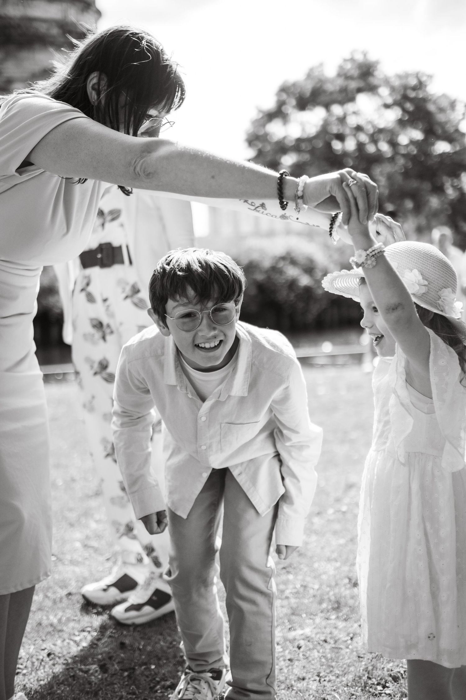 Black and white photo of children in white attire playing outdoors with an adult during a celebration.