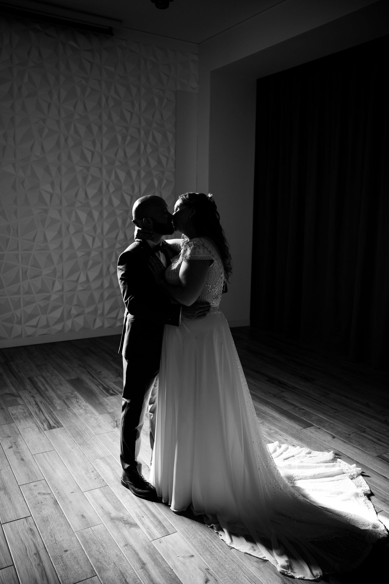 Black and white photo of a bride and groom sharing a romantic kiss on a wooden dance floor.