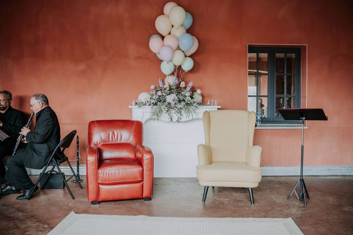 Red recliner and cream wingback chair arranged for a wedding ceremony with balloon decor and a musician playing flute.