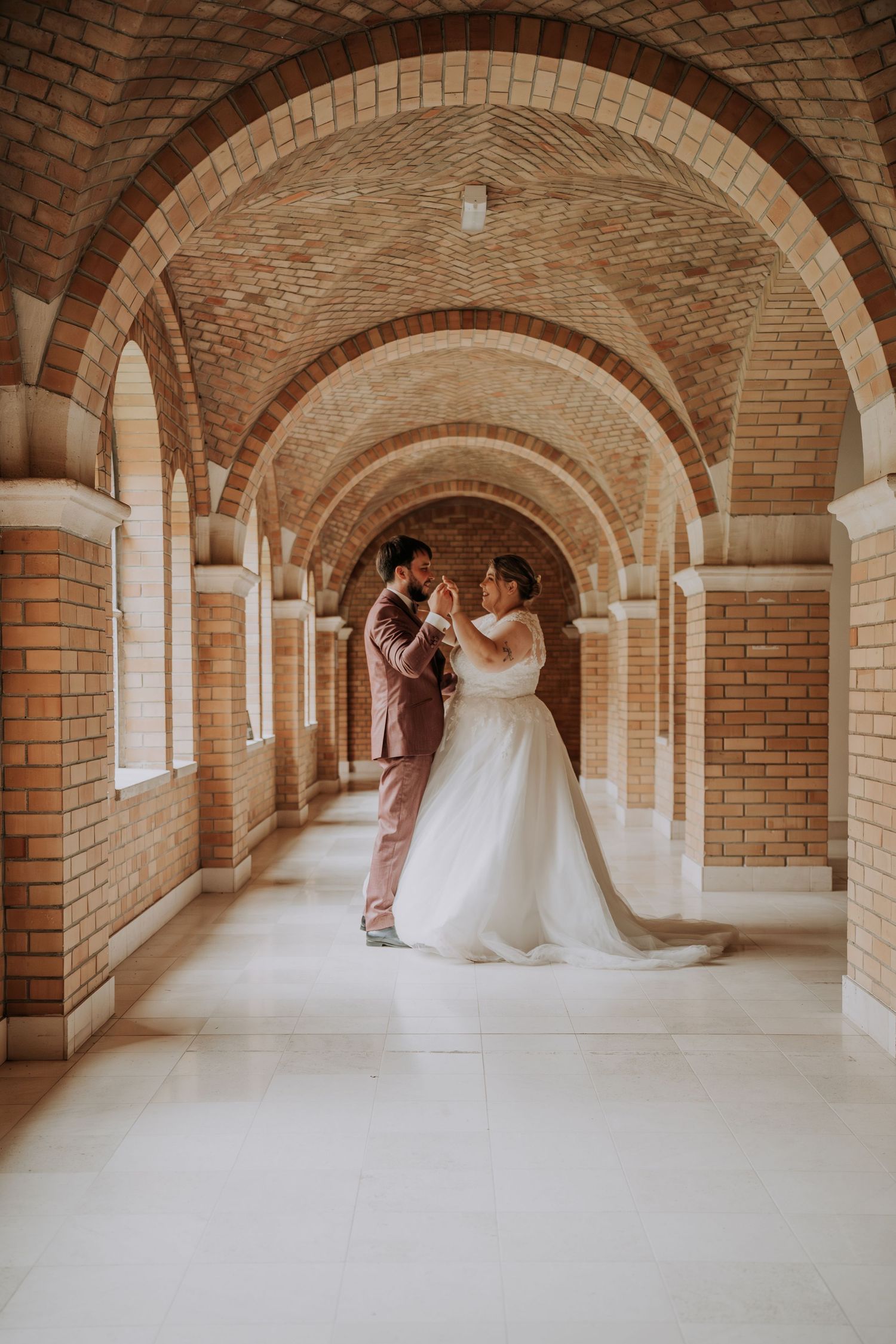 Bride and groom dancing in an elegant brick archway corridor, showcasing a stunning white ball gown wedding dress.