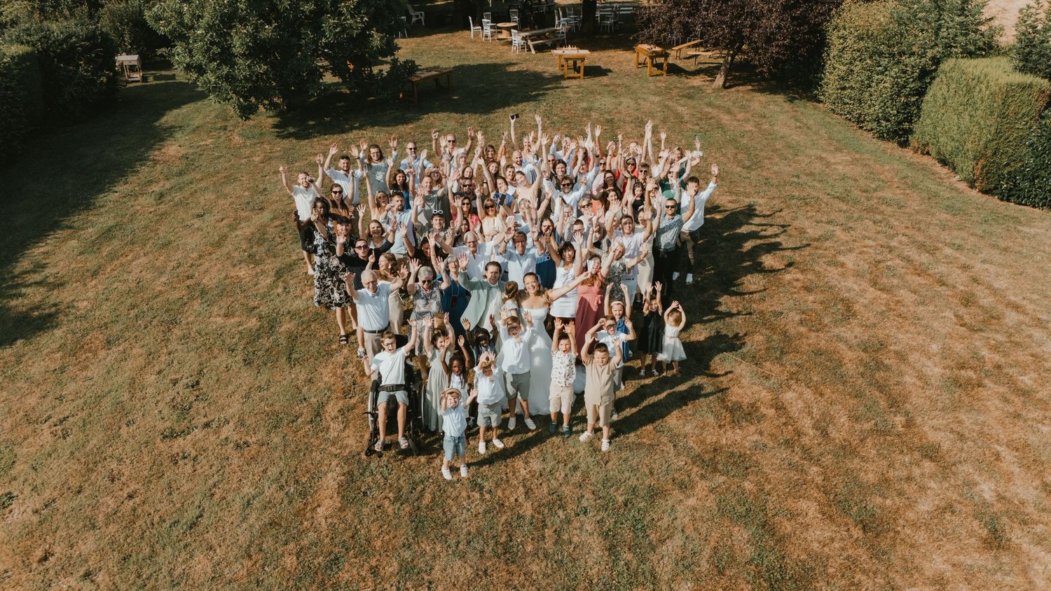 Aerial view of a large group of people celebrating outdoors on a green lawn, raising their arms joyfully.