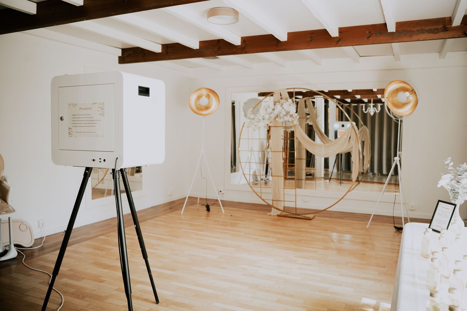 Elegant wedding photo booth setup with gold globe decor, wooden floor, and white walls in a rustic venue.