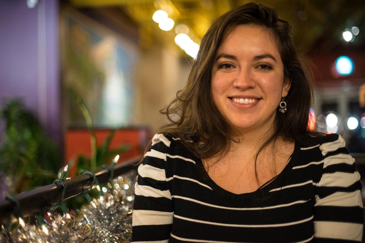 A woman in striped shirt smiles warmly at camera in evening lighting.