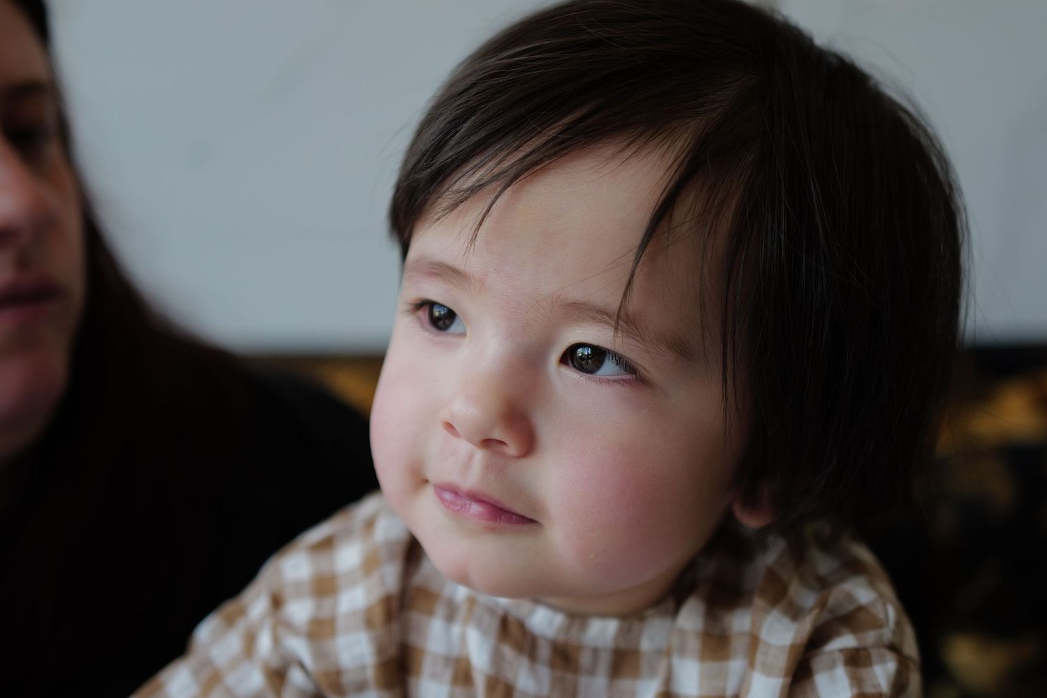 A young child in a checkered shirt looks to the side with a gentle expression.