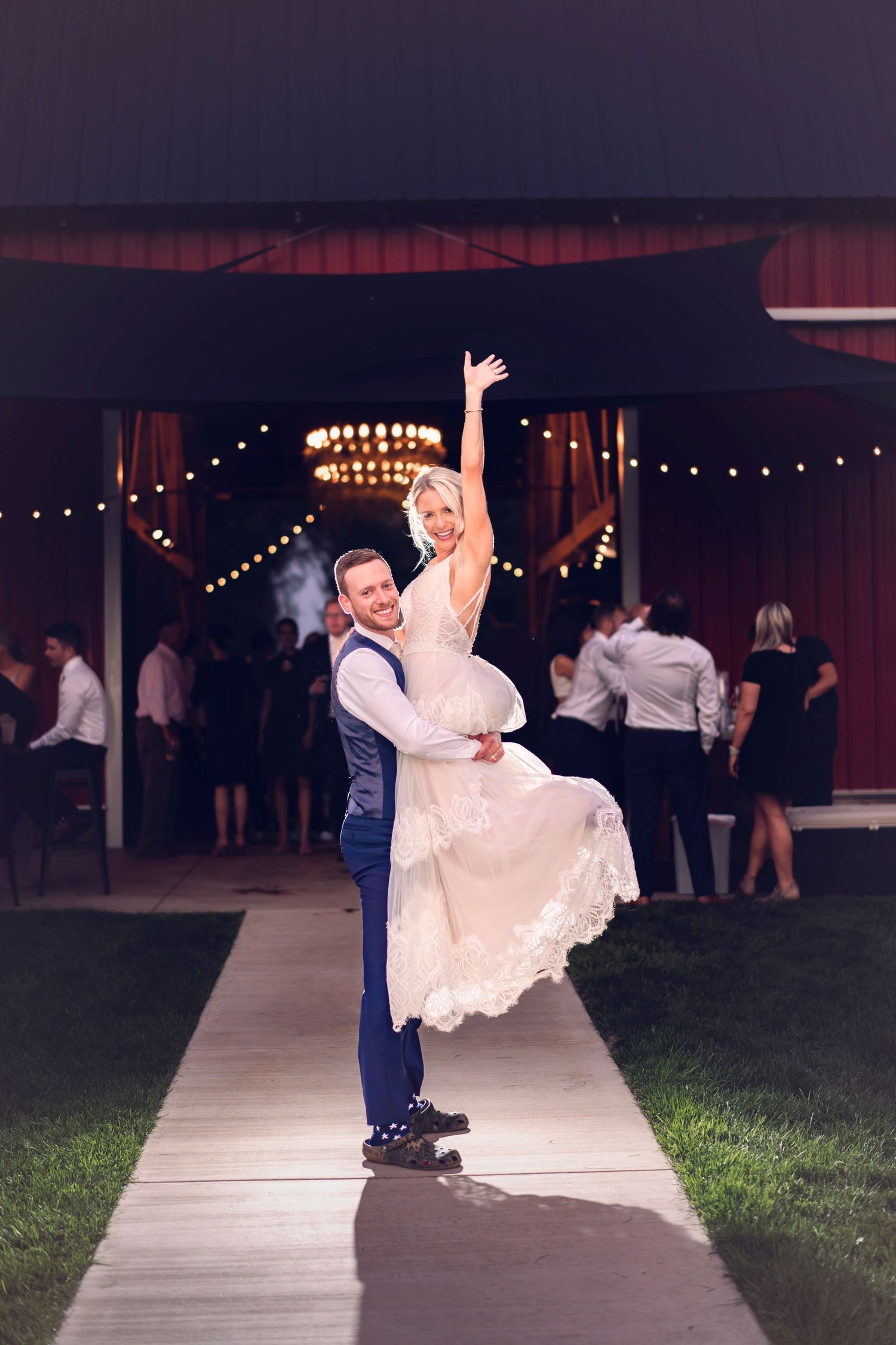 A celebratory end of the night wedding day photo of the groom holding the bride in joy.