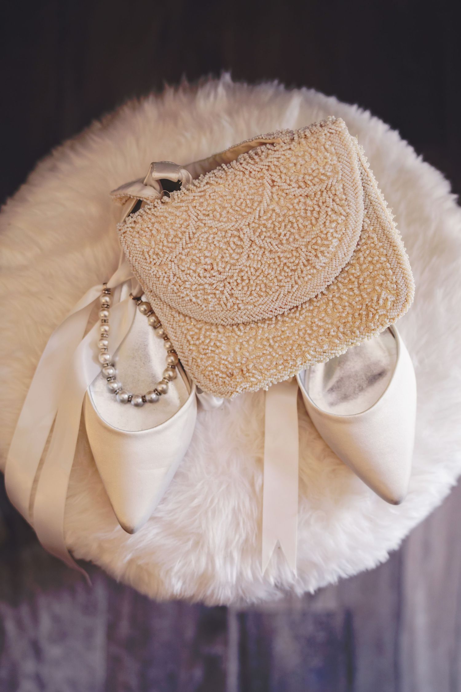 An antique beaded purse rests atop ivory wedding shoes on a faux fur ottoman at The Blue Heron Barn in Kalamazoo, Michigan.