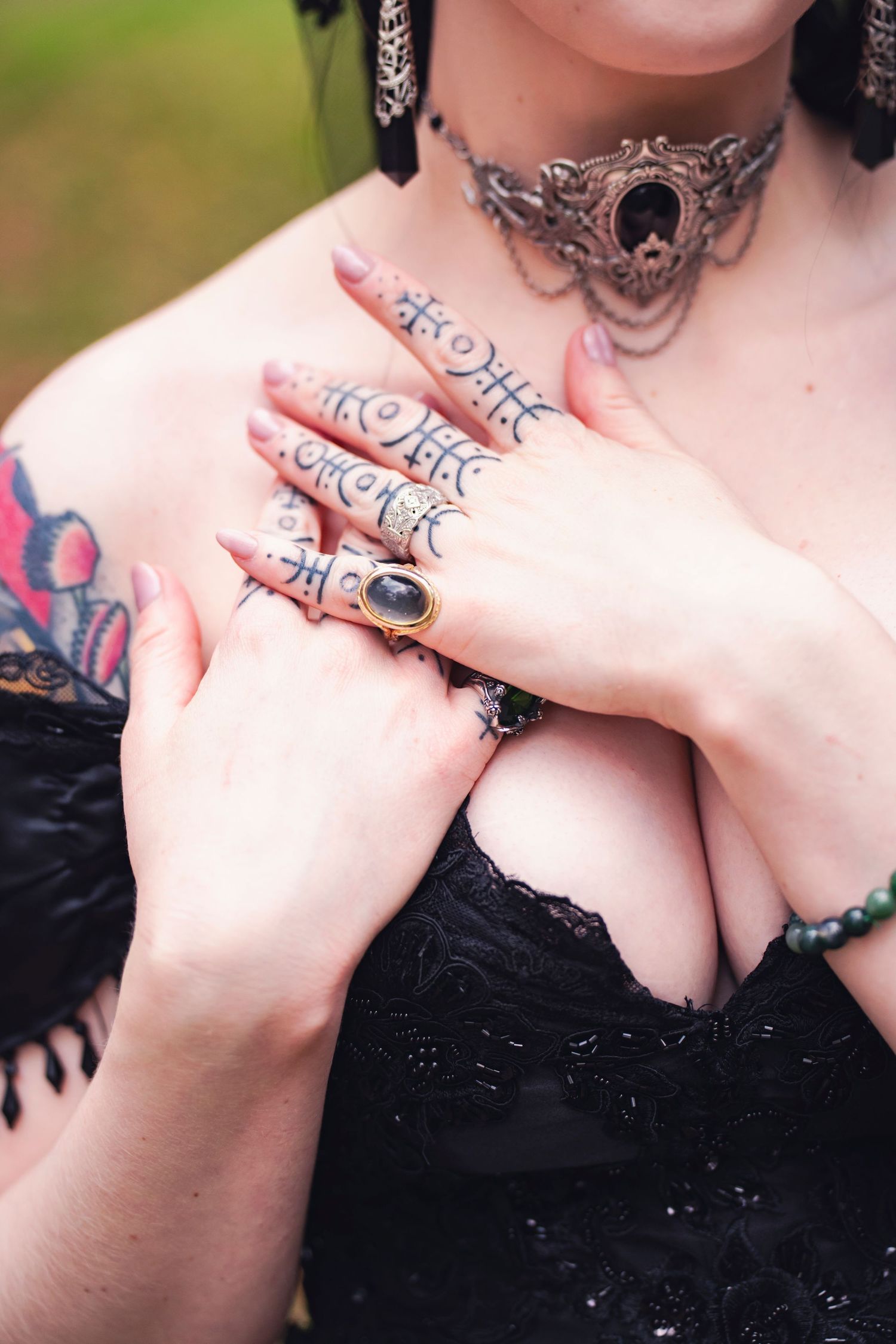 A gothic bride at a Halloween-themed wedding wears an ornate choker and an antique onyx ring. She is elegantly posed to show finger tattoos.