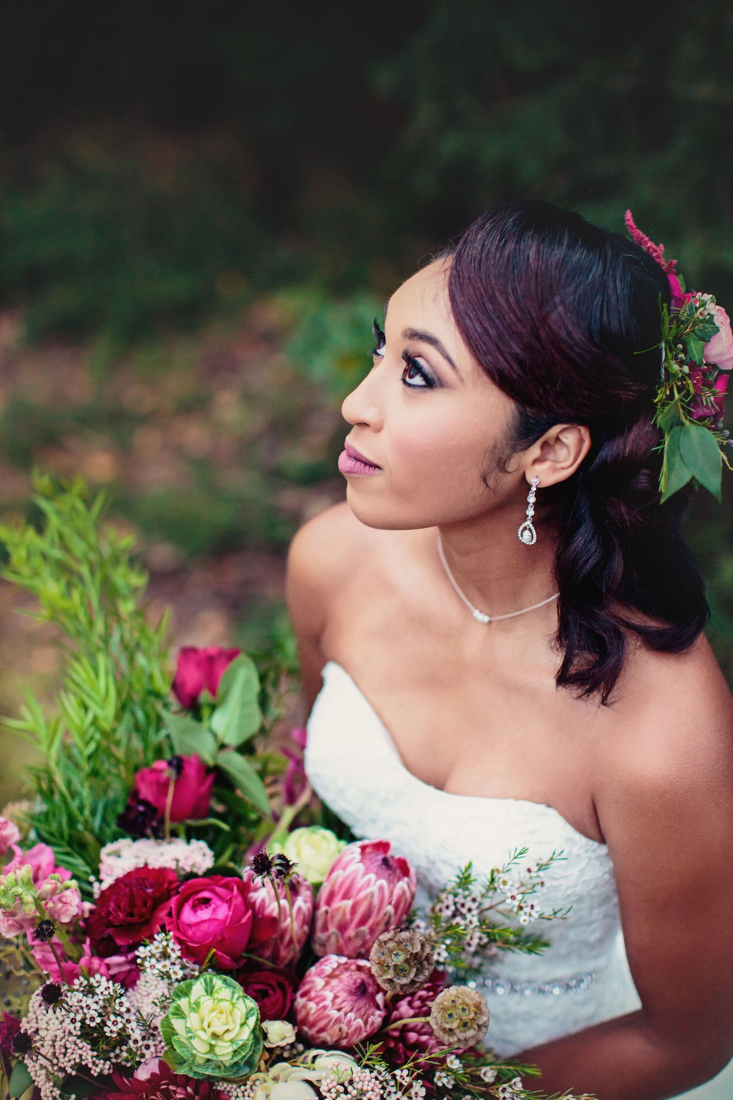 A bride holding an oversized rustic boho wedding bouquet showcasing makeup and jewelry.