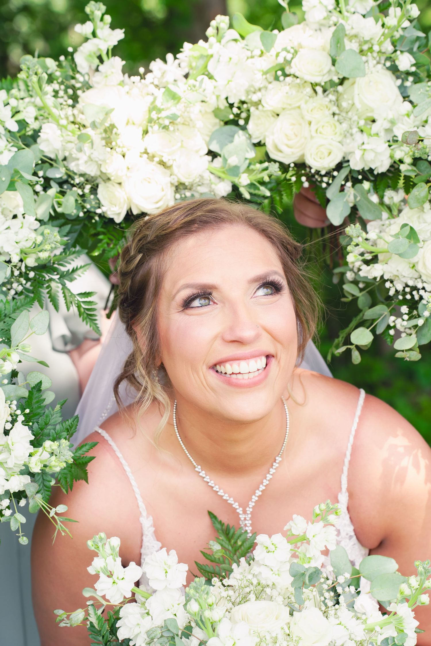 The face of a bride smiling with joy surrounded by her bridesmaids' bouquets on her wedding day at Twin Gables Event Center in Sturgis, MI.