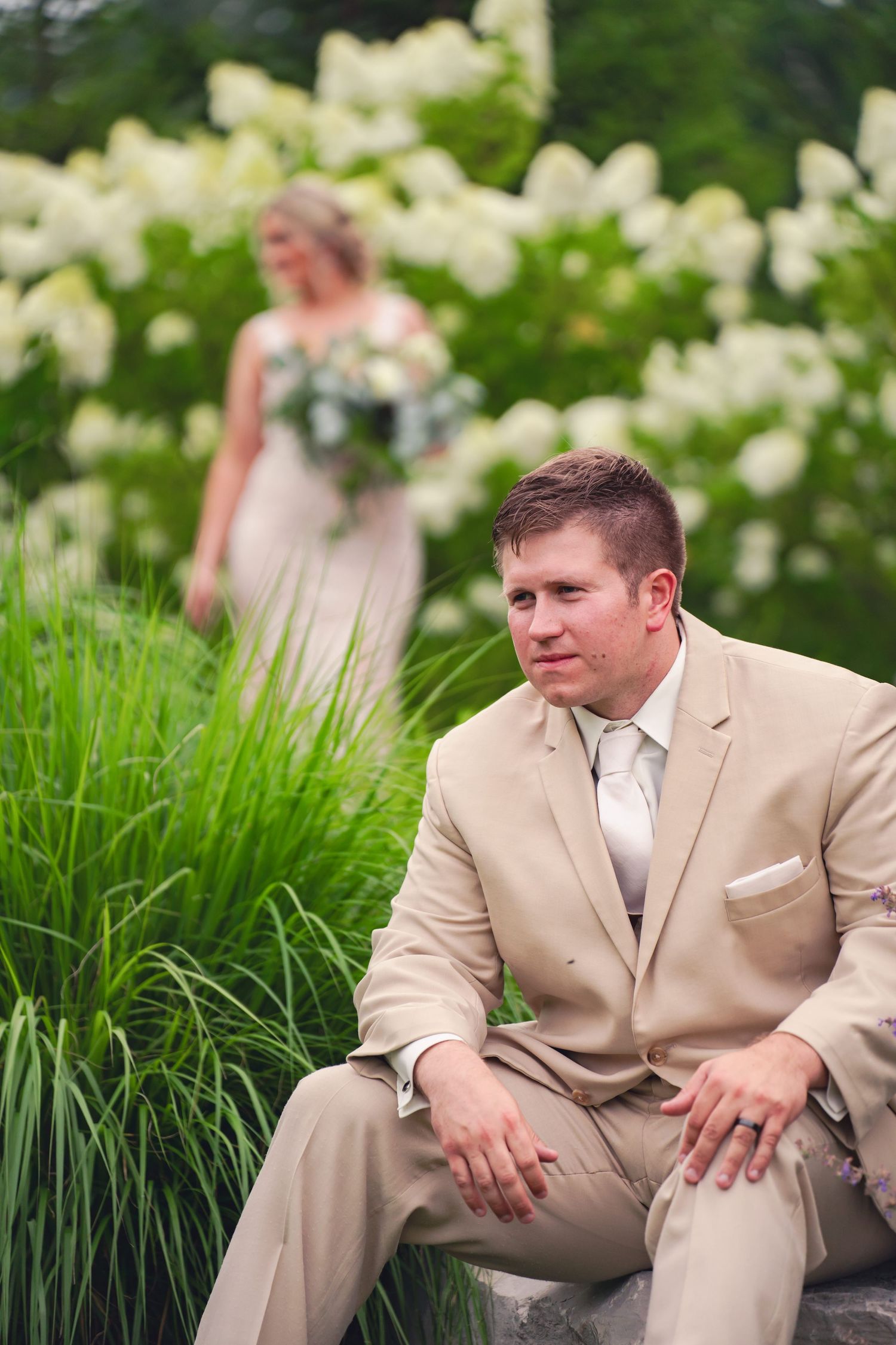 A artistic photo of groom sitting in the foreground while his bride is seen in the background in shallow depth of field.