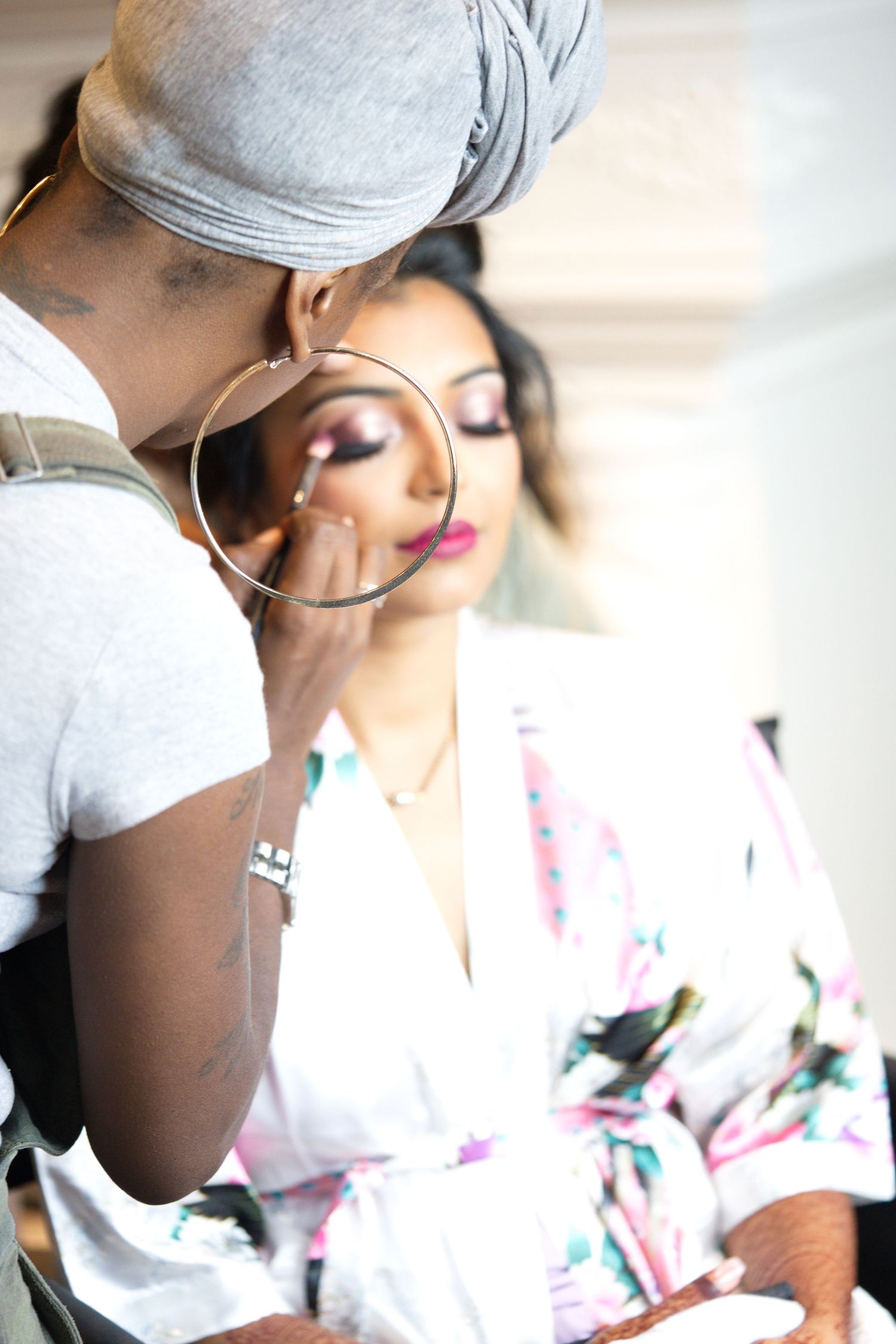 A creatively framed photo of a South East Asian bride having her makeup done by a Black makeup artist on the morning of her wedding day.