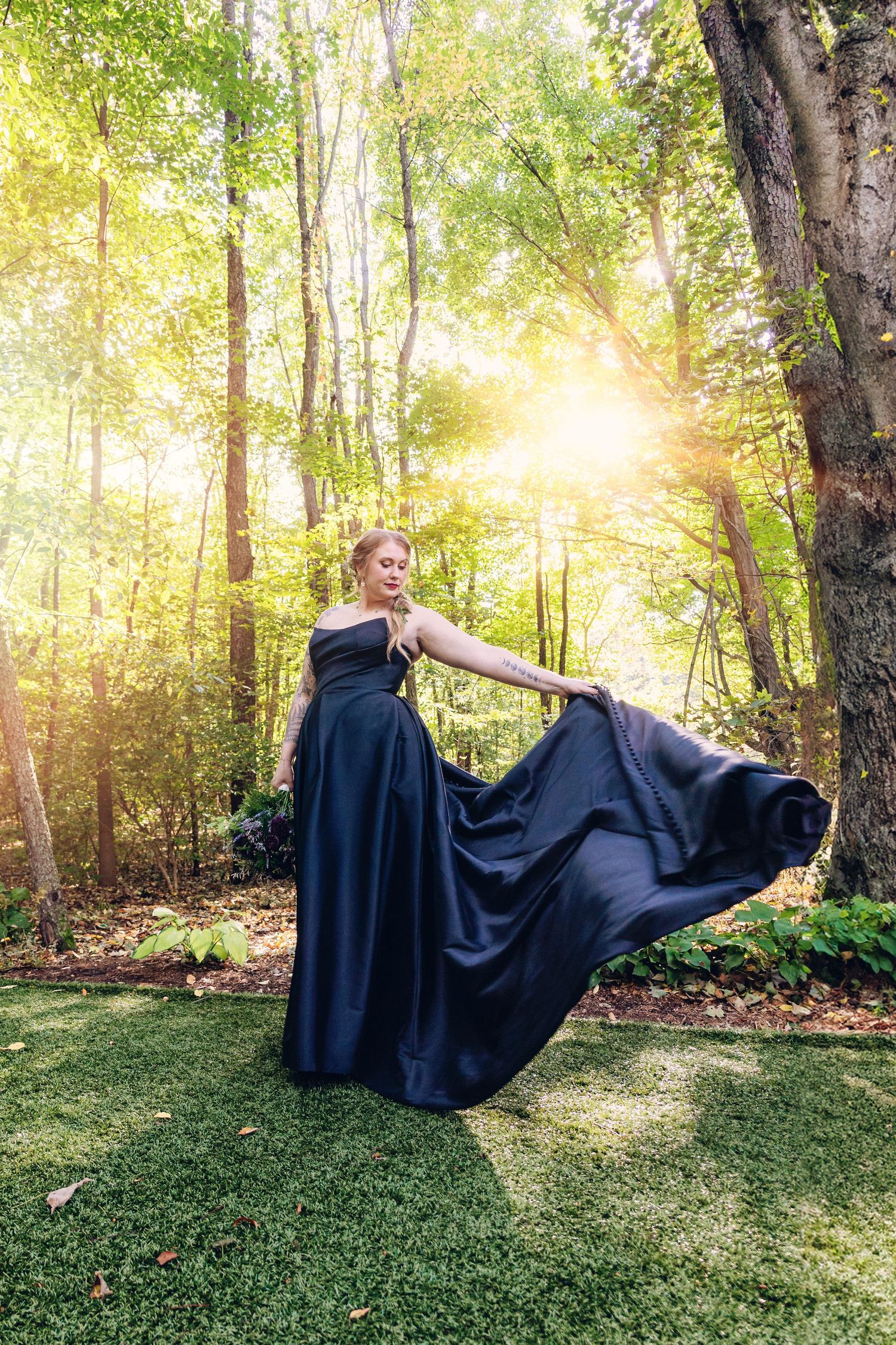 A bride in a black gown gracefully lifts the satin skirt of her dress, creating a smooth, flowing wave as the fabric catches the light.