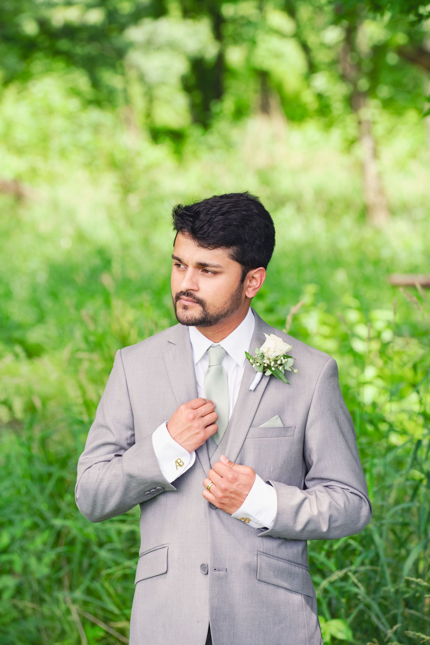 A groom adjusts his lapel in front of a grassy field at Twin Gables Event Center in Sturgis, Michigan.