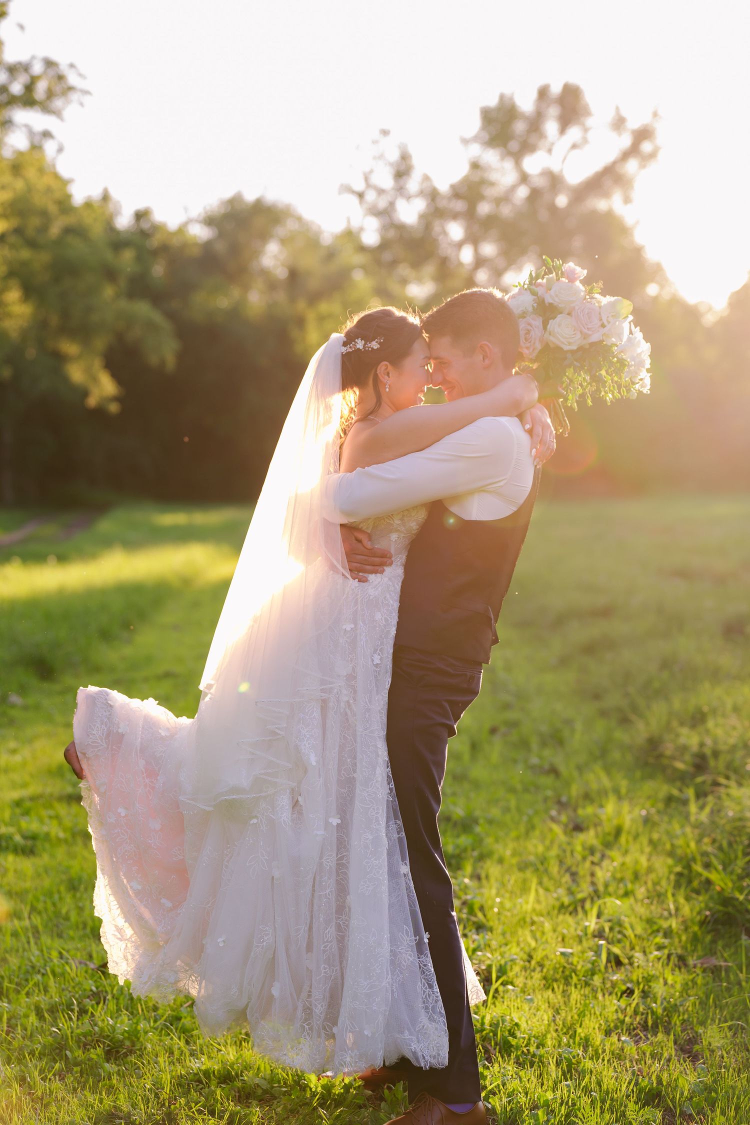 A groom picks up his bride in a sunlight field behind Blue Heron Barn.
