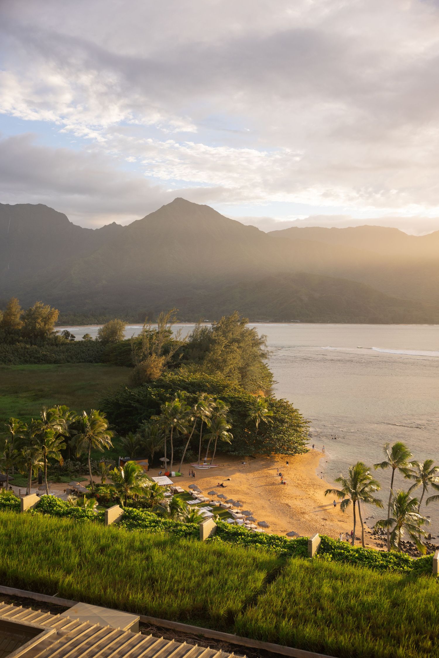Sunrise over a tropical beach with mountains, palm trees and beachfront cottages in Hawaii.