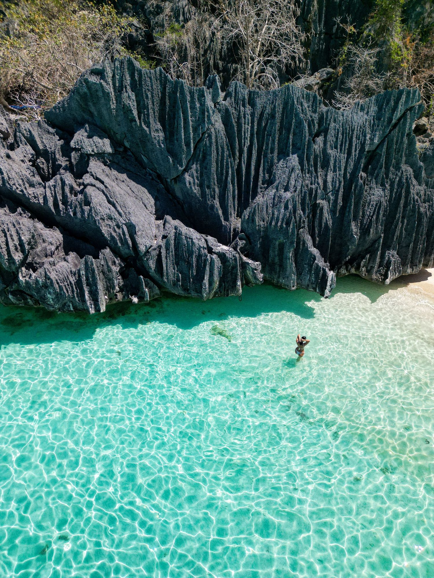 Aerial view of crystal clear turquoise waters and dramatic limestone cliffs at secluded beach.