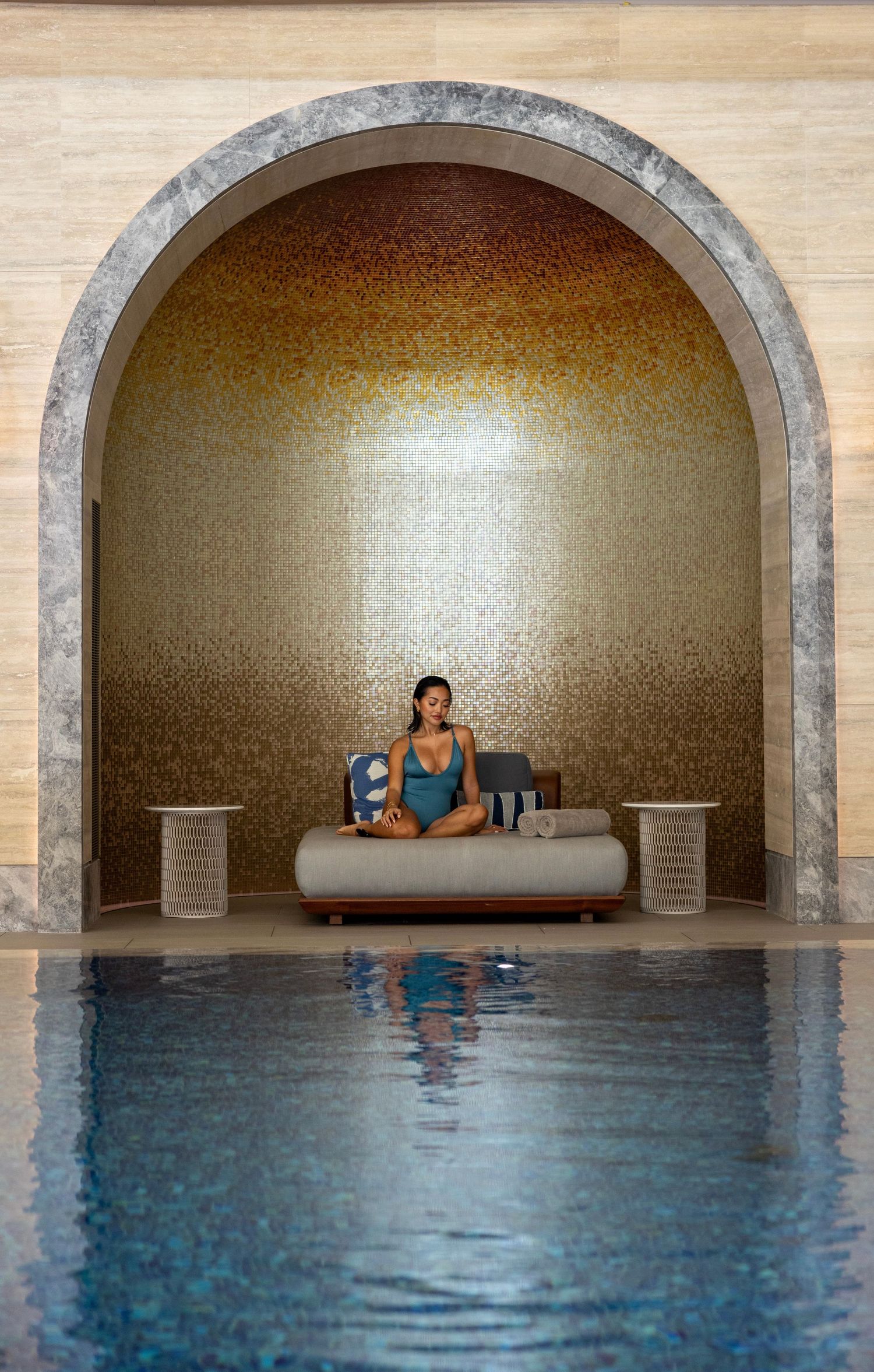 Indoor pool with illuminated arched alcove and water reflection at a luxury spa.