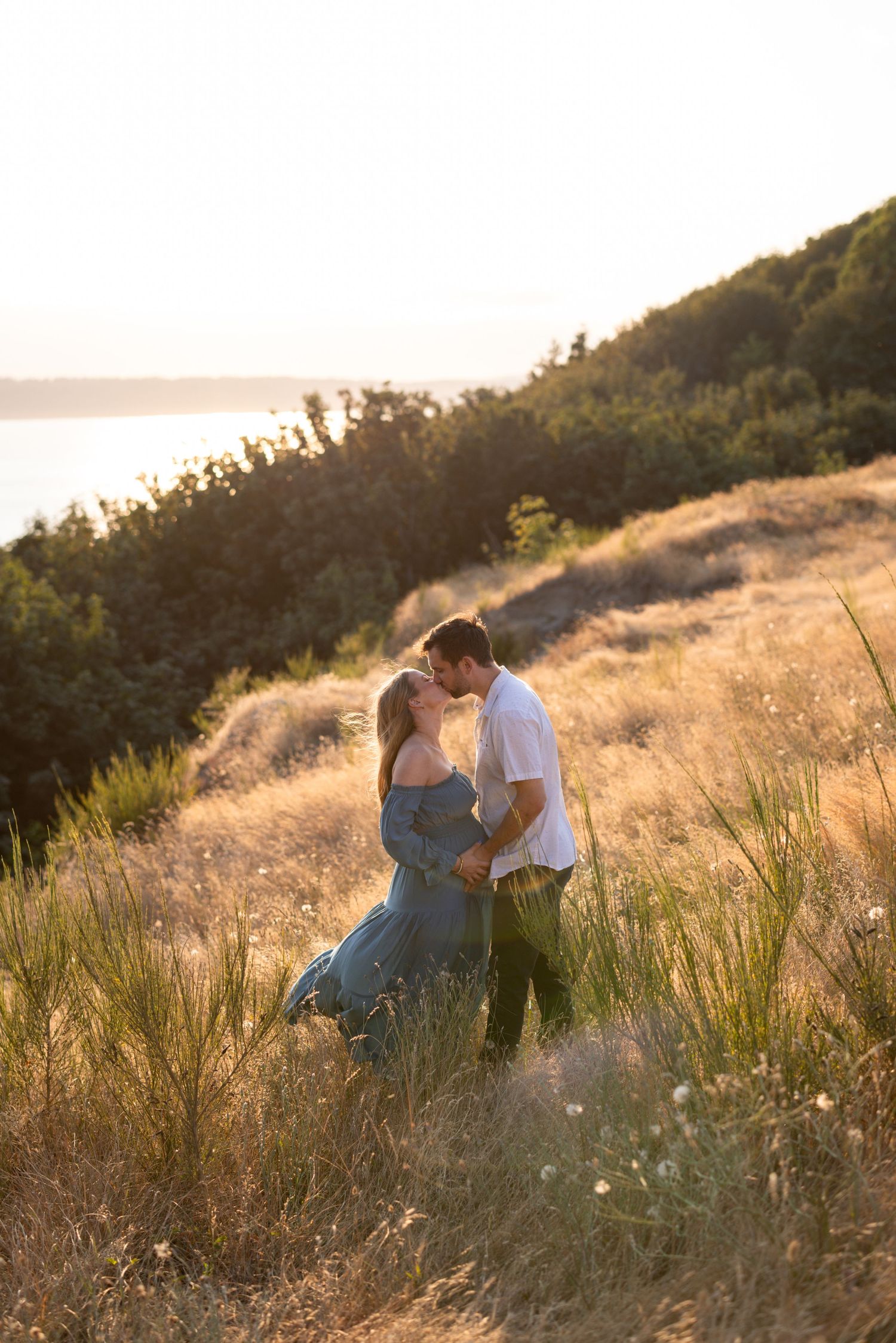 Couple sharing intimate moment in golden sunset light on grassy hillside.