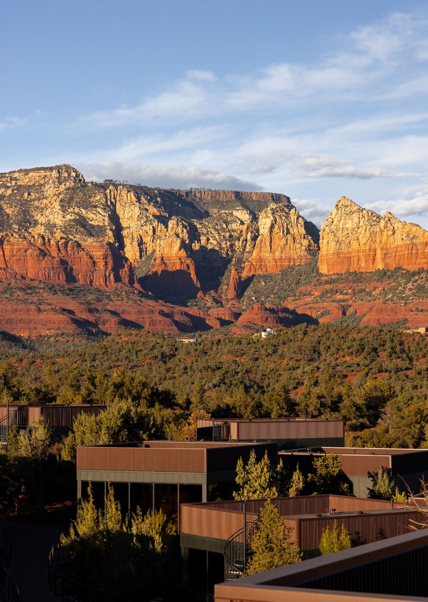 Modern buildings set against dramatic red rock formations of Sedona at sunset.