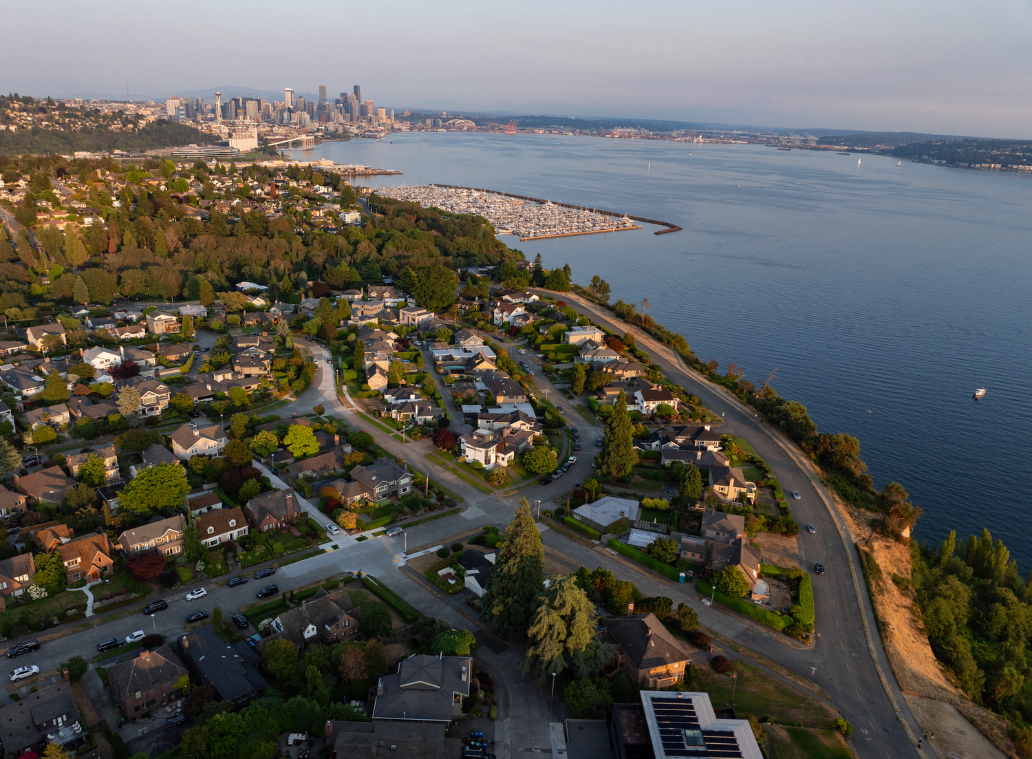 Coastal residential area with waterfront homes overlooking a scenic bay and city skyline.