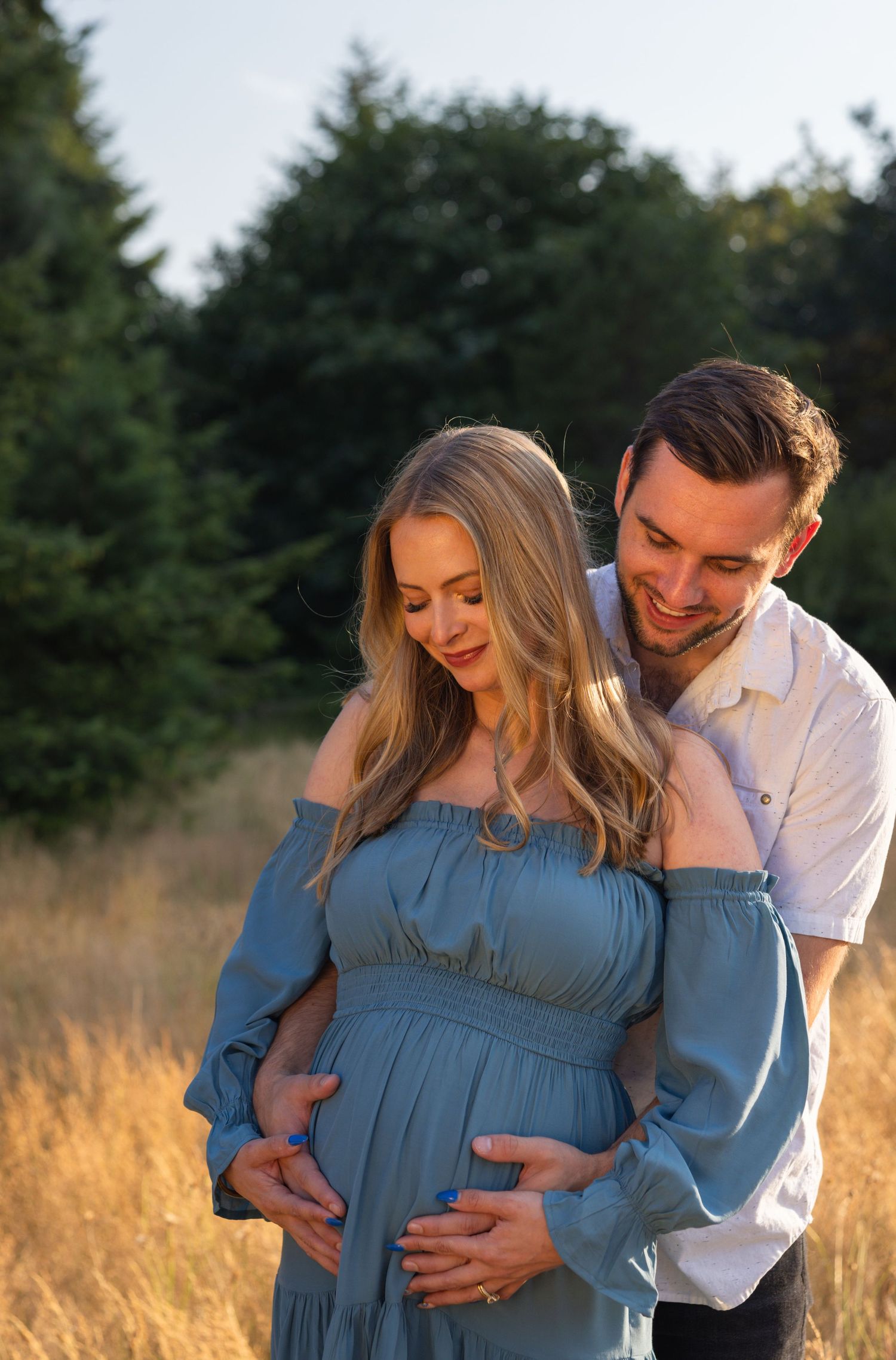 Joyful maternity portrait of couple embracing in sunlit meadow.