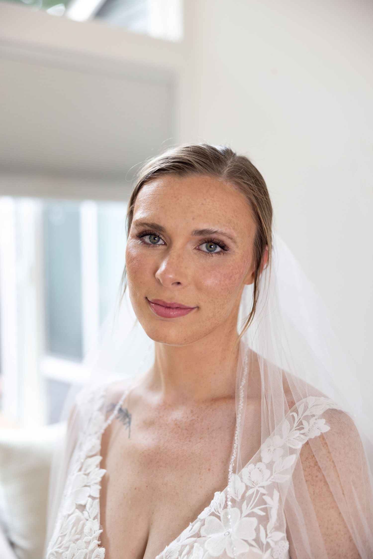 Elegant bride wearing delicate lace wedding dress and veil in natural window light.