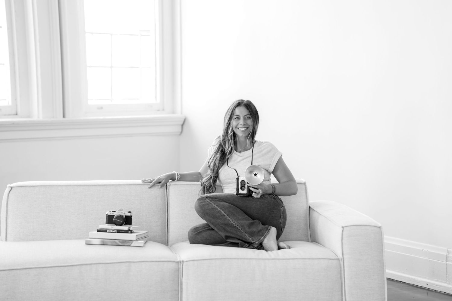 Person lounging on a white couch while reading a book in a bright, minimalist room.