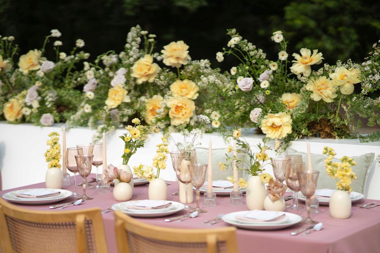 Elegant wedding table setting with yellow roses and white floral centerpieces on a long banquet table.