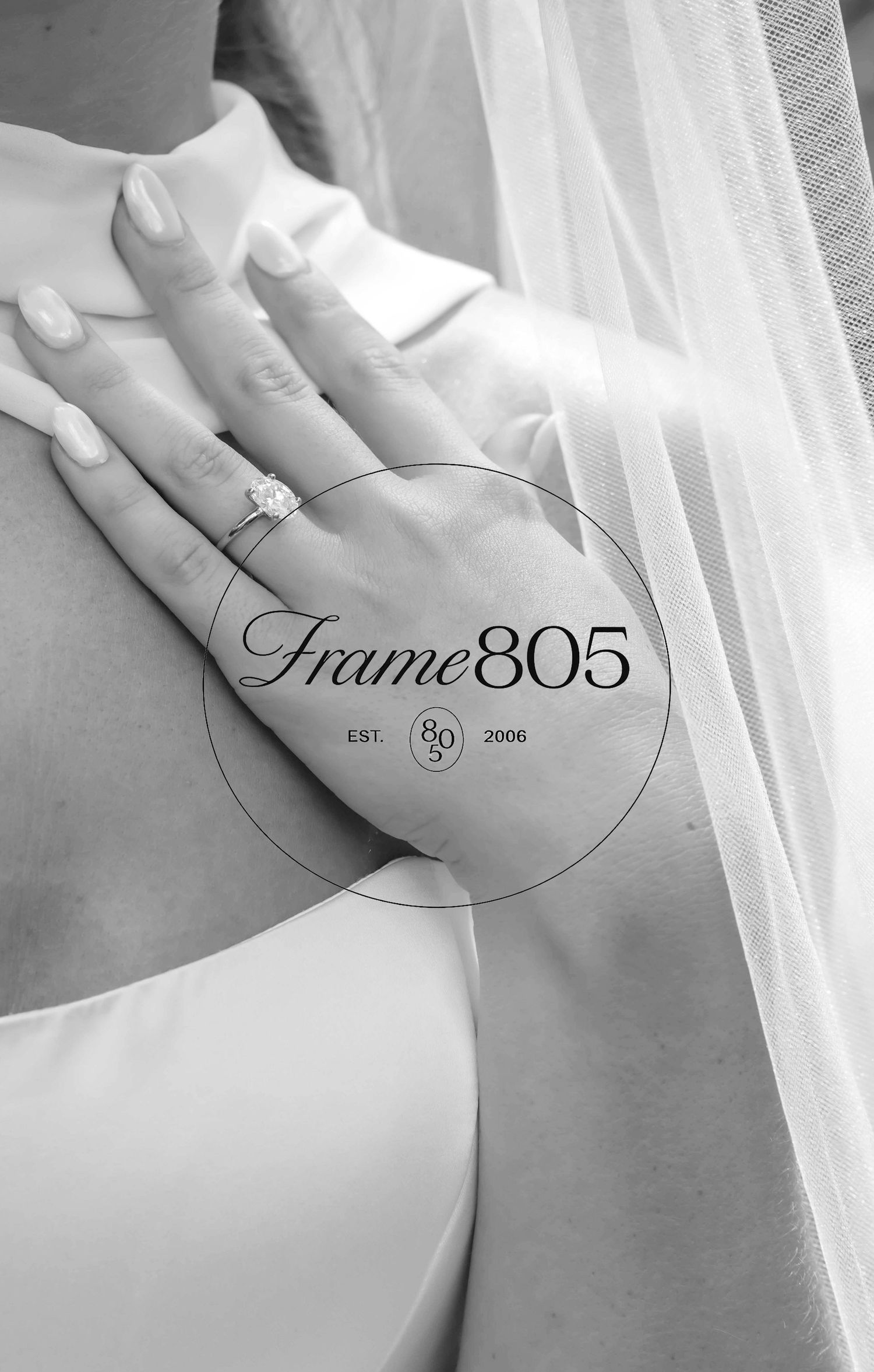 Black and white photo showing a diamond engagement ring on a hand against white fabric with Frame805 logo overlay.