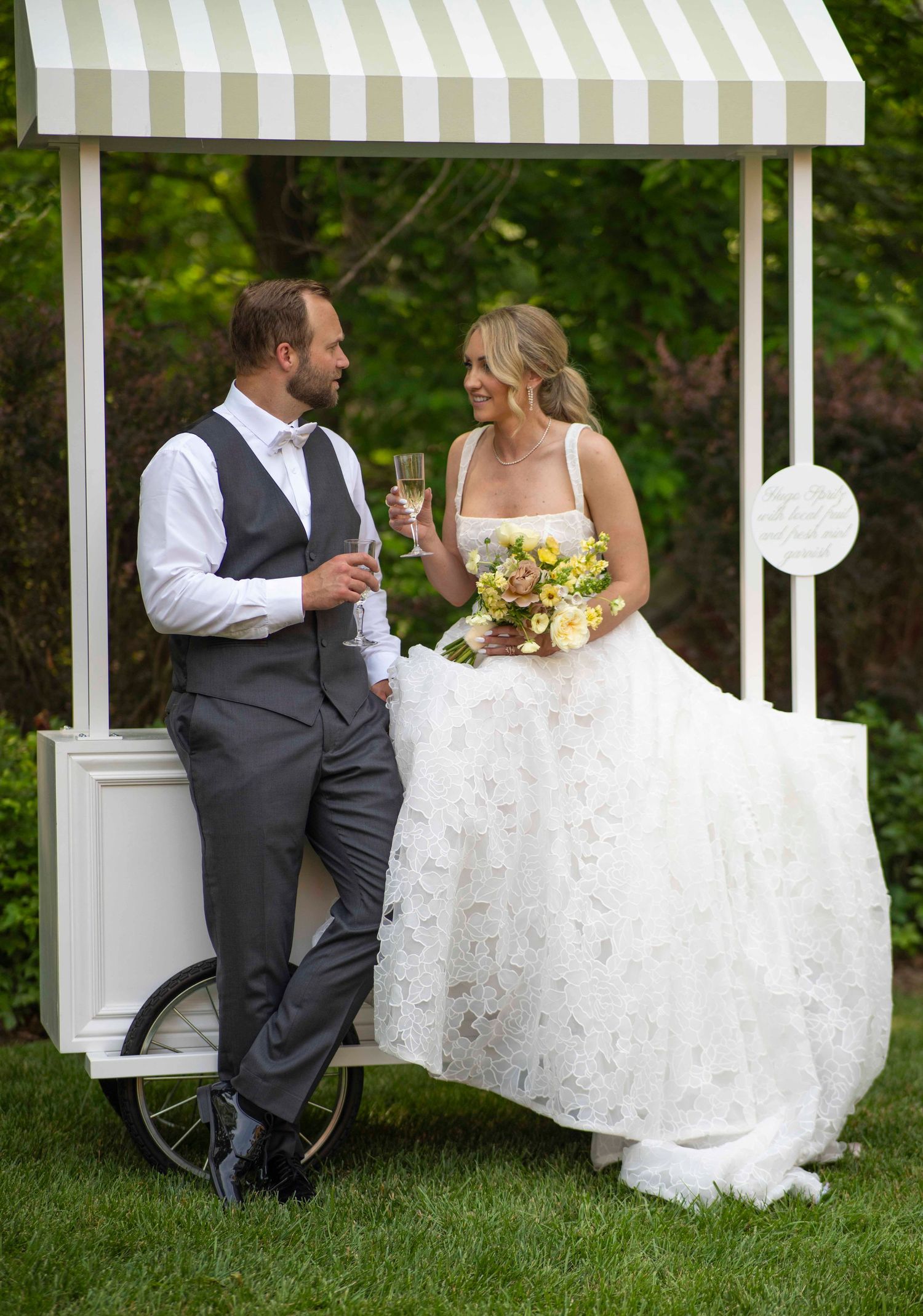 Bride and groom share an intimate moment sitting together on white chairs in a lush garden setting.
