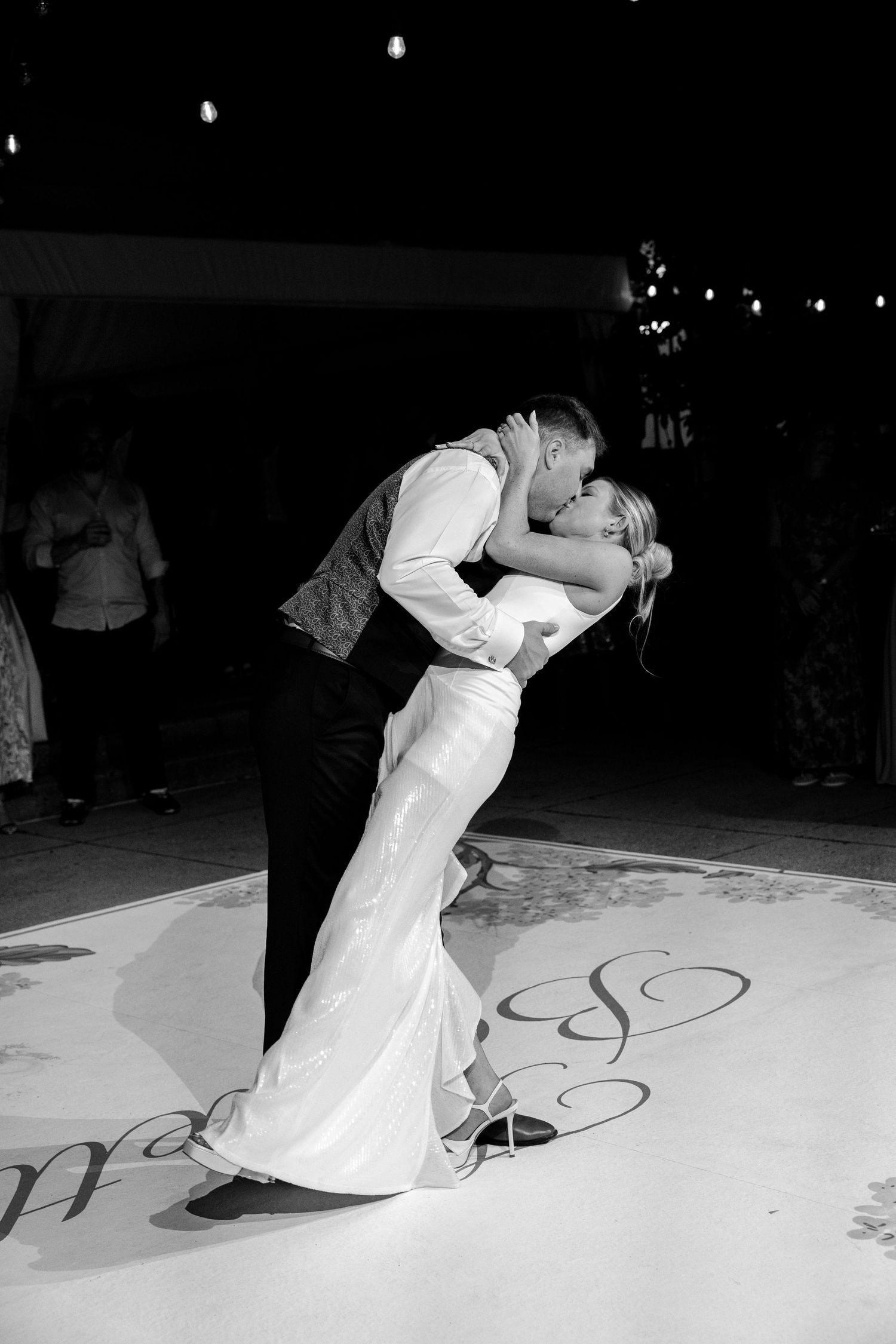 Black and white photo of bride and groom sharing a romantic dip kiss during their first dance at wedding reception.