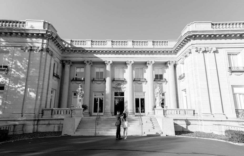 Black and white photograph of a grand neoclassical building entrance with white columns and ornate architectural details.