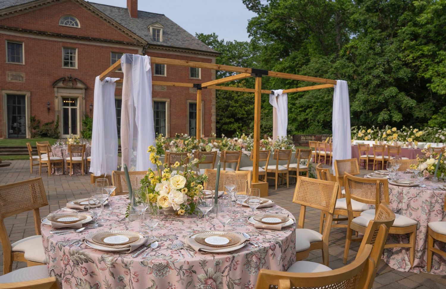 A panoramic view of an elegant outdoor wedding reception setup with floral tablescapes and white umbrellas.